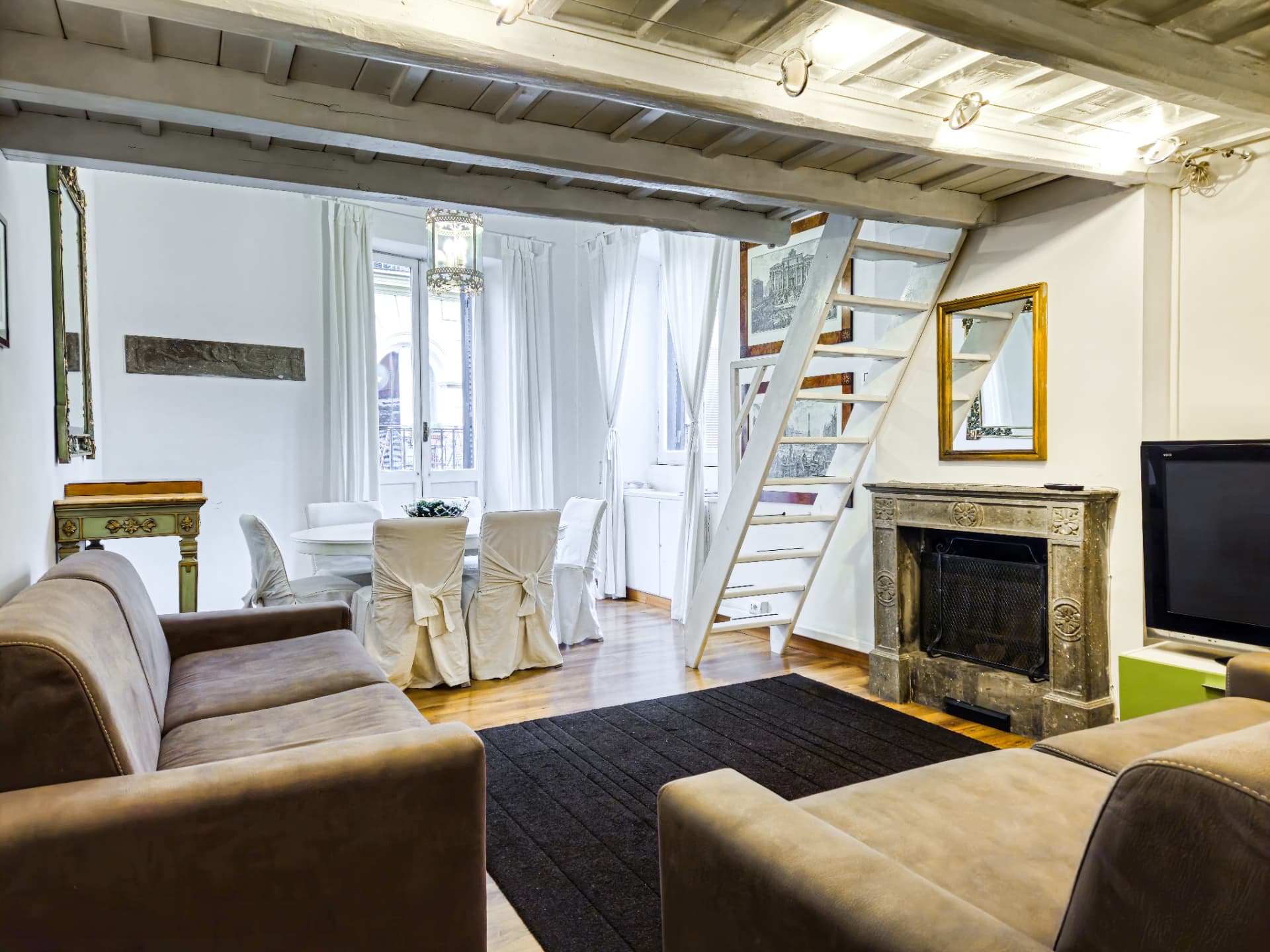 Soggiorno e sala da pranzo con soffitto a travi, camino e scala per il soppalco